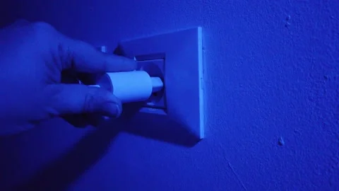 Against a blue background, a hand inserts a charger into a socket Stock Footage 296234948