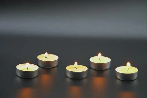 Against a dark background , five small white tea light candles are burning Stock Photos