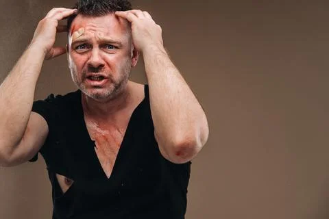Against a gray background stands a battered angry man in a black T-shirt with Stock Photos