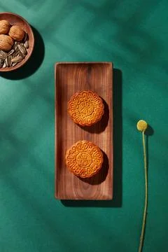 Against the green background with shadow of window, two wooden trays of moonc Stock Photos