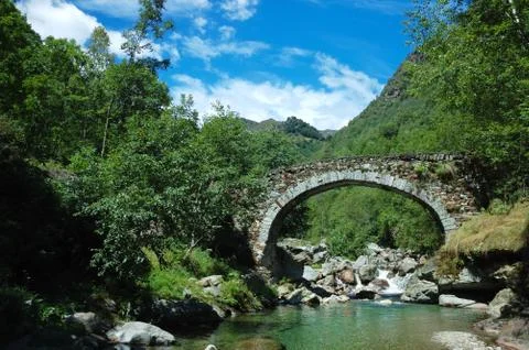 Aged arch bridge over a small mountain river Stock Photos
