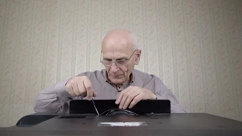 Aged bald man unscrews outdated black television set cover Stock Footage 125599475