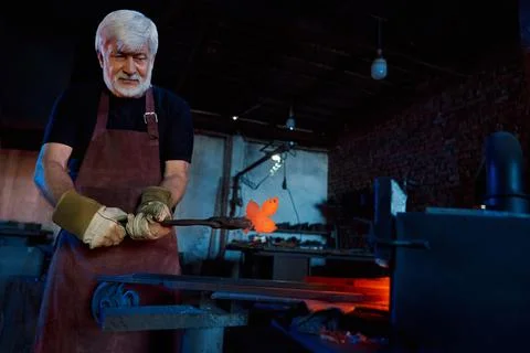 Aged blacksmith working at forge with heated metal Stock Photos