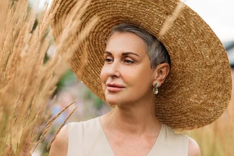 Aged female in a straw hat looking at wheat Stock Photos
