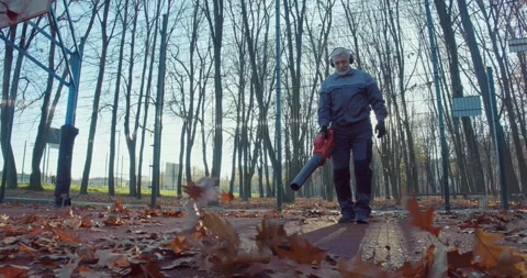 Aged gardener using leaf blower while cleaning city park Stock Footage 257805206