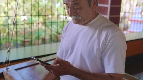 Aged Indian male using mobile phone in a rural traditional house  Stock Footage 341515345
