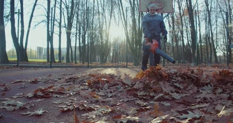 Aged janitor using leaf blower for cleaning autumn park Stock Footage 251805410