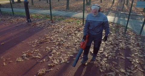 Aged janitor using leaf blower for cleaning autumn park Stock Footage 253194270