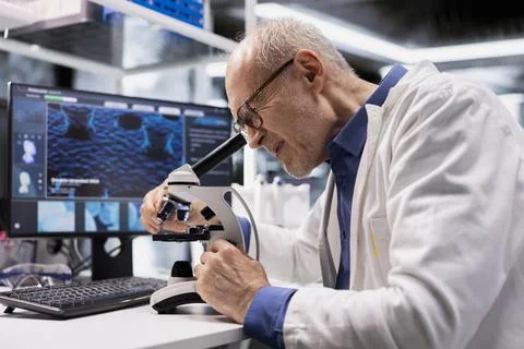 Aged laboratory expert at microscope analyzes bioscience samples on a tray Stock Photos