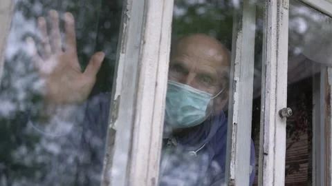 Aged man in blue disposable face mask touching glass of window with hand. Stock Footage 145086406