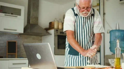 Aged man cleans his hands of the dough and uses a computer to read instructions Stock Footage 156494299