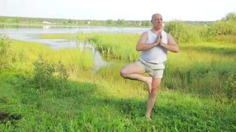 Aged man doing stretching exercises on the lake in the morning. 库存影片 115908099