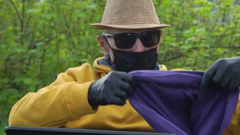 Aged man in mask takes pullovers comparing with online shop Stock Footage 130836336