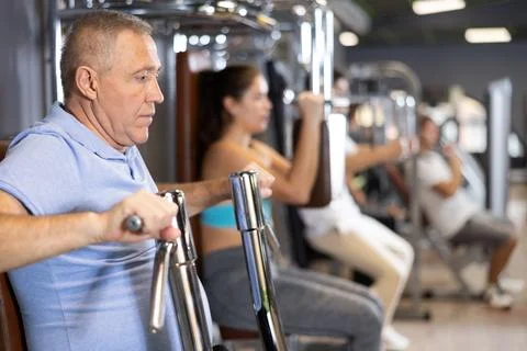 Aged man performing chest press in exercise machine in gym Stock Photos