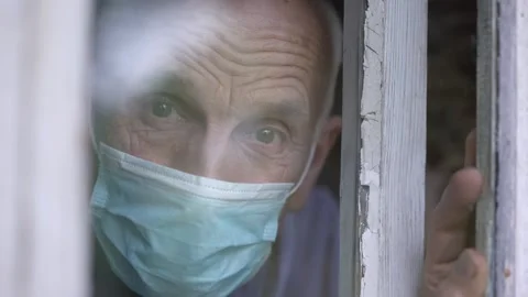 Aged man in protective facemask looking with sorrow through window glass Stock Footage 144132309