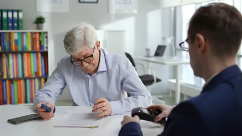 Aged man read agreement and pay insurance fee with credit card in modern company Vidéo 175149883