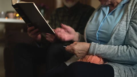 Aged man reading book and talking with wife knitting scarf, family leisure time Video stock 315869130