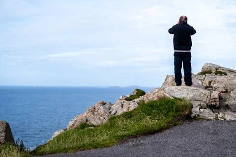 Aged man standing on the cliff using binoculars Stock Photos