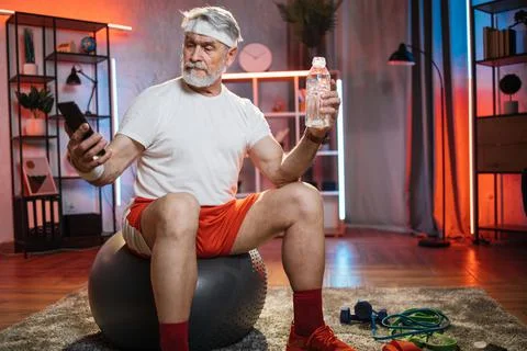 Aged man taking selfie on mobile while sitting on fitball Stock Photos