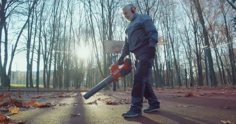 Aged man in uniform using leaf blower for cleaning park Stock Footage 257805374