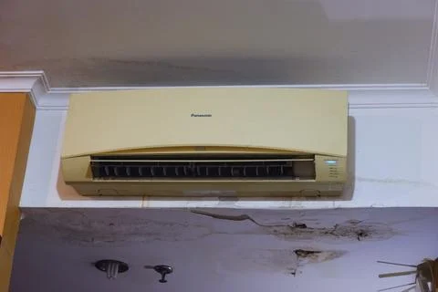Aged Panasonic Split Air Conditioner Mounted on Damaged Interior Wall Stock Photos