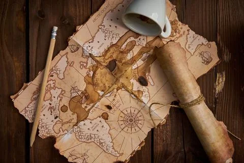 Aged parchment scroll, an old map, a pencil, and a spilled coffee cup on a woode Stockfoto's