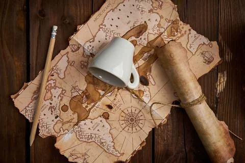 Aged parchment scroll with an old map and a spilled coffee cup on a wooden table Stockfoto's