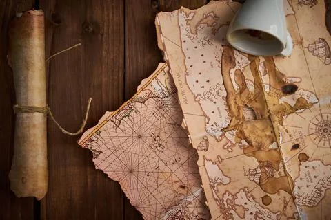 Aged parchment scroll with old maps and a spilled coffee cup on a wooden table. Stockfoto's