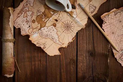 Aged parchment scroll with old maps and a spilled coffee cup on a wooden table. Stockfoto's