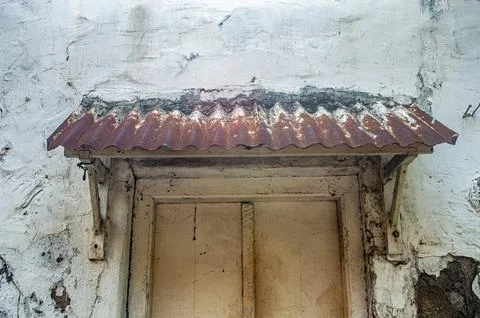 An aged, peeling white wall frames a vintage wooden door beneath a rusty co.. Stock Photos