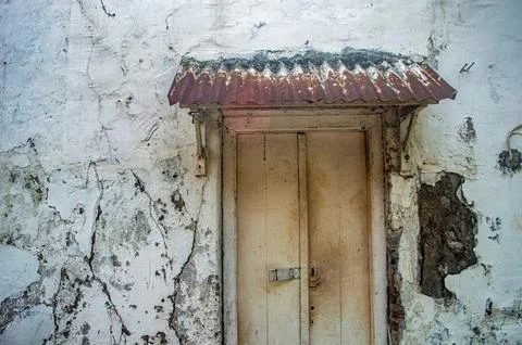 An aged, peeling white wall frames a vintage wooden door beneath a rusty co.. Stock Photos
