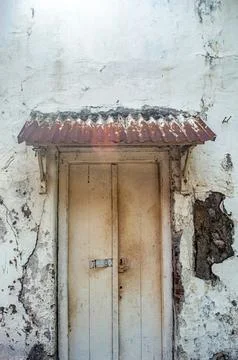 An aged, peeling white wall frames a vintage wooden door beneath a rusty co.. Stock Photos