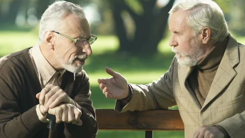 Aged pensioner with hearing problem listening to friend, sitting on park bench Stock Footage 99877075