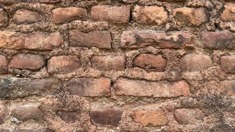 Aged rough brick wall surface with uneven mortar exhibits historical characte Stock Photos