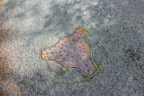 An aged, rusted triangular manhole cover with rounded edges is embedded in a  Foto stock