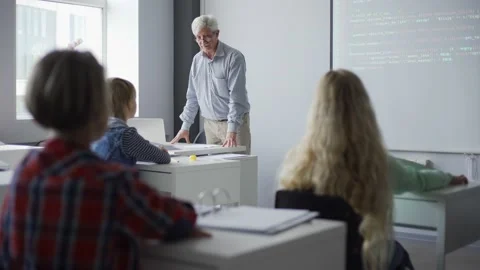 Aged teacher explaining computer programming to students using projector scre Stock Footage 142491218