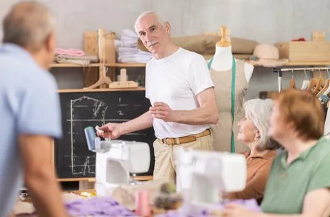 Aged teacher explaining pattern structure by chalkboard during sewing course for 스톡 사진