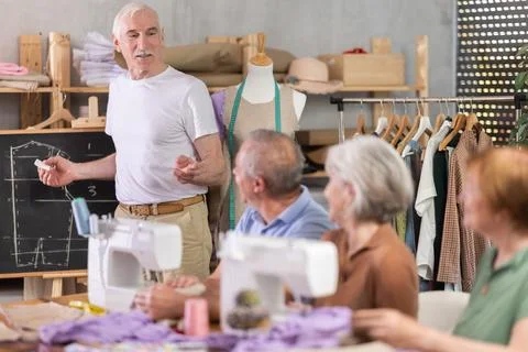 Aged teacher explaining pattern structure by chalkboard during sewing course for 스톡 사진