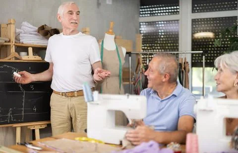 Aged teacher explaining pattern structure by chalkboard during sewing course for 스톡 사진