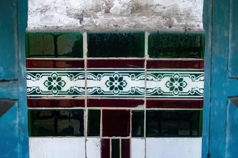 An aged wall column features vibrant green and maroon patterned tiles, fram.. 스톡 사진