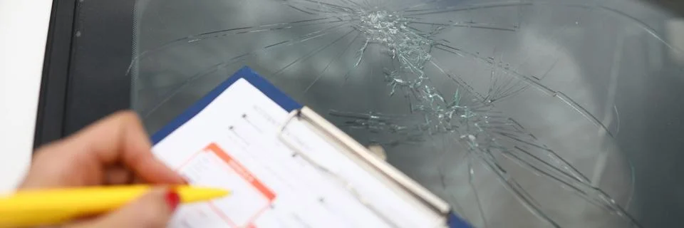 An agent draws up documents for broken windshield in car. Stock Photos