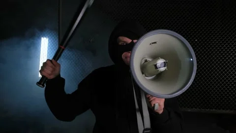 An aggressive activist in a balaclava and with a bat shouts into a megaphone Stock Footage 168828014