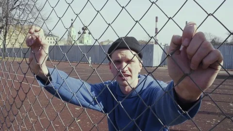 Aggressive caucasian man talking something on a sports field behind metal fence Video stock 74516870