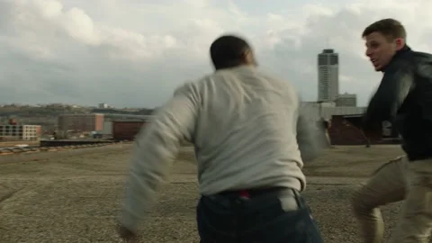 Aggressive man punches and knocks down a weaker man on a warehouse rooftop in ov Stock Footage 199460479