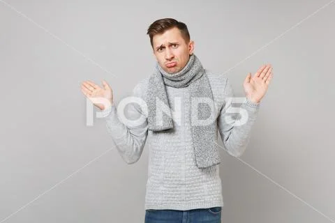 Aggrieved young man in gray sweater, scarf pouting lips, spreading hands Stock Photos