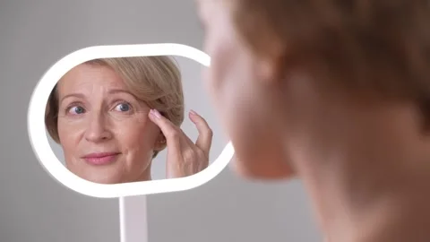 Aging female looking at skin changes in mirror Stock Footage 291836790