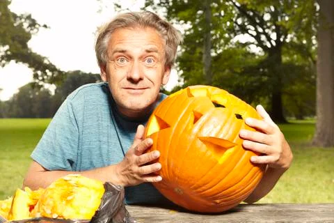 Aging man in city park preparing funny helloween pumpkin Stock Photos