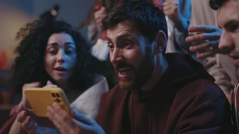 Agitated guy rejoicing while watching over sports betting at the smartphone Stock Footage 169098905
