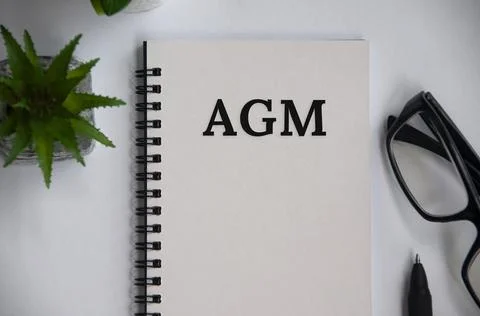 AGM text on notepad with glasses and plant background. Conceptual Stock Photos
