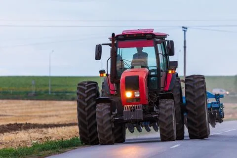 Agricultural tractor moving on the asphalt road after working in field Stock Photos